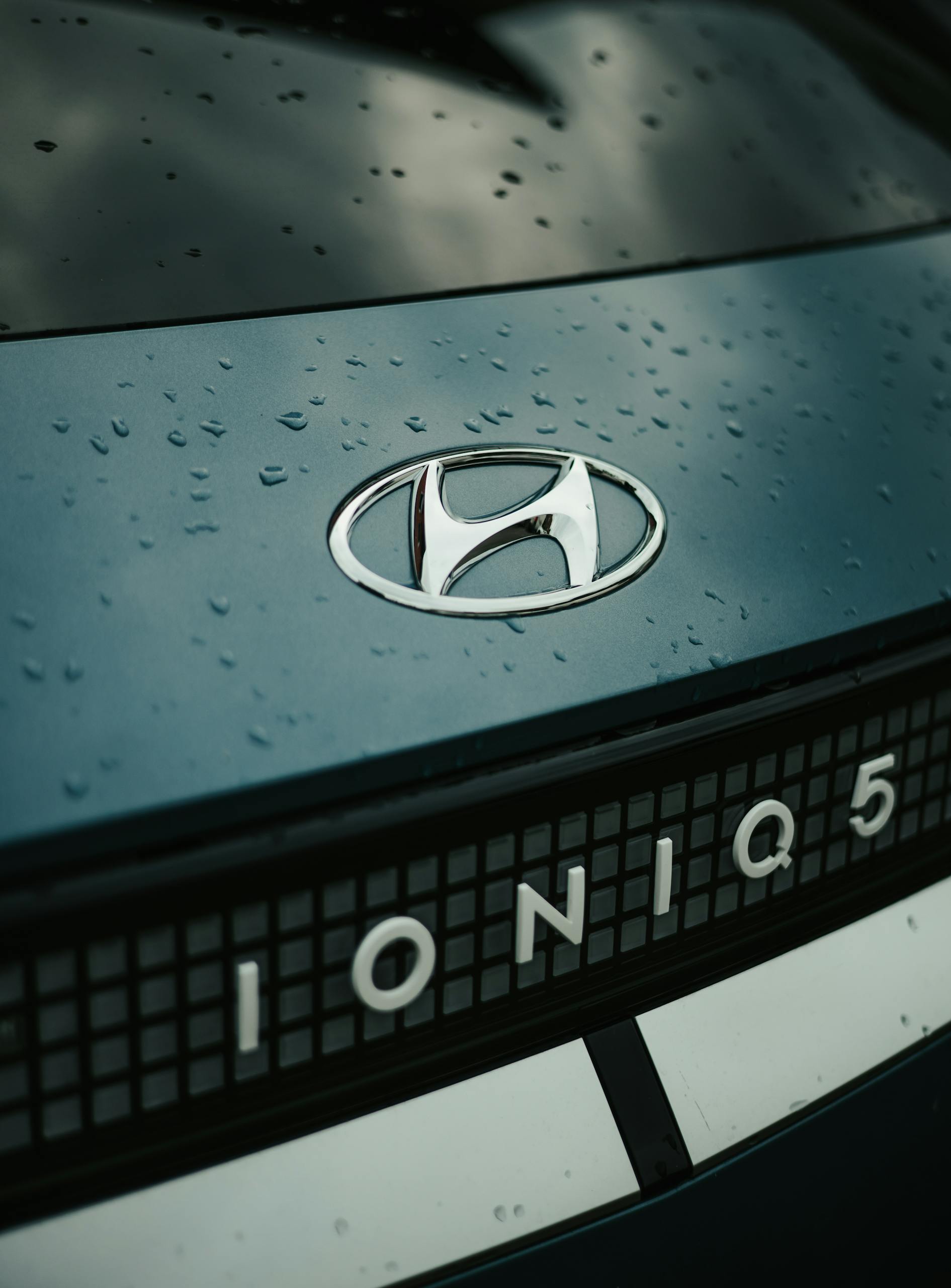 Close-up of Hyundai Ioniq 5 emblem with raindrops, showcasing sleek design and branding.